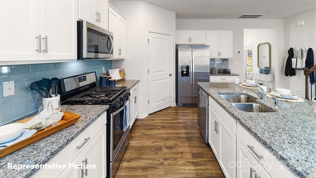 kitchen with appliances with stainless steel finishes, a sink, light stone countertops, dark wood finished floors, and white cabinetry