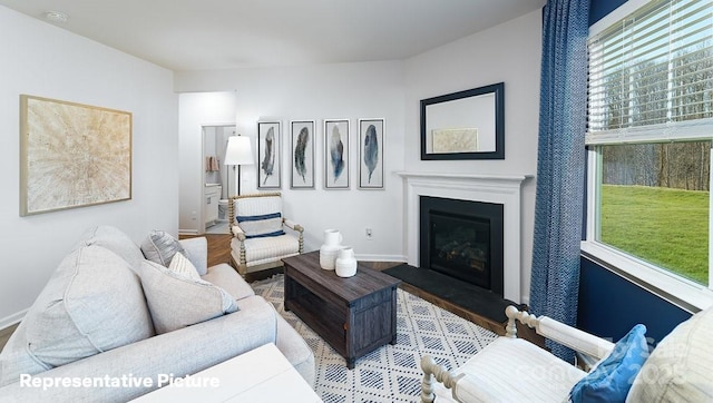 living area featuring baseboards, a glass covered fireplace, and wood finished floors