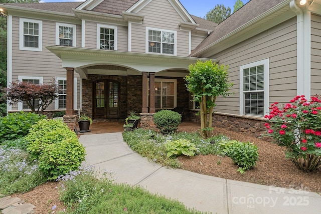 doorway to property featuring a shingled roof, covered porch, and stone siding