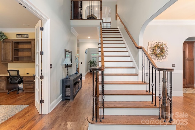 stairway featuring crown molding, arched walkways, baseboards, and wood finished floors