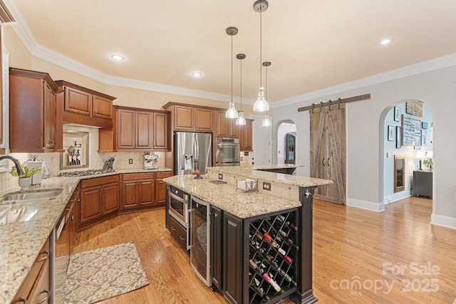 kitchen with brown cabinets, a sink, light wood finished floors, arched walkways, and stainless steel appliances