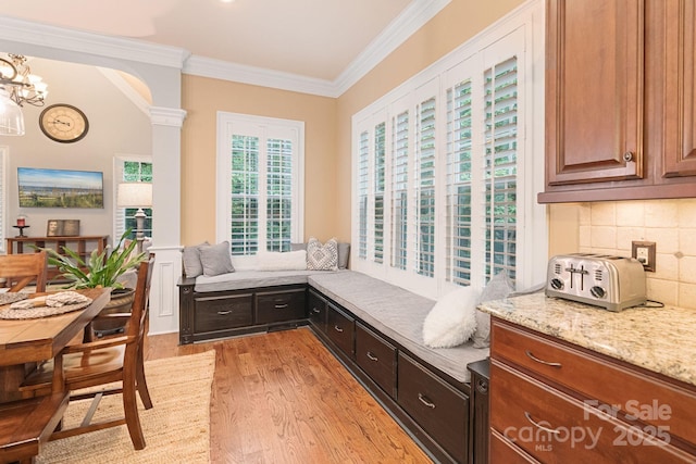 sitting room featuring crown molding, an inviting chandelier, arched walkways, light wood-style flooring, and ornate columns