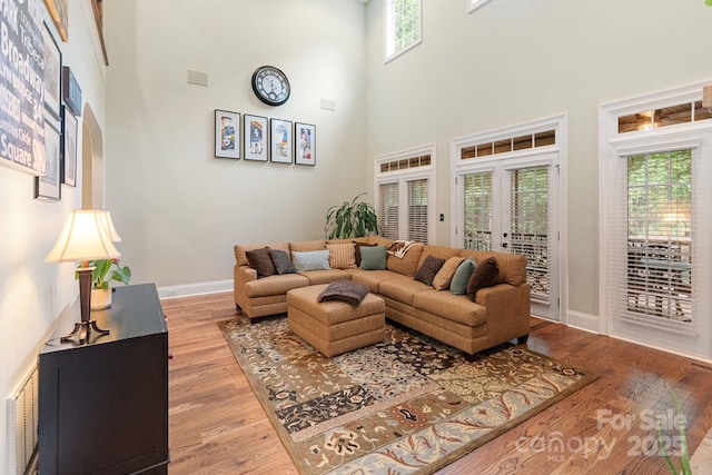 living area with visible vents, light wood-style floors, baseboards, a high ceiling, and french doors