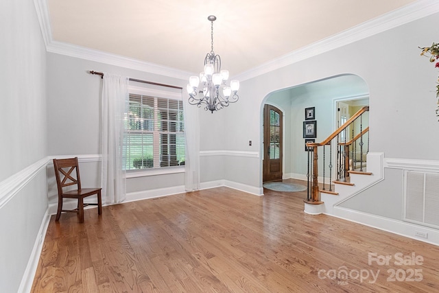 unfurnished dining area featuring visible vents, arched walkways, wood finished floors, a chandelier, and ornamental molding