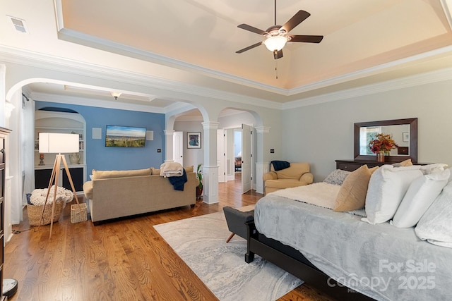 bedroom with visible vents, arched walkways, light wood-type flooring, a raised ceiling, and ornate columns