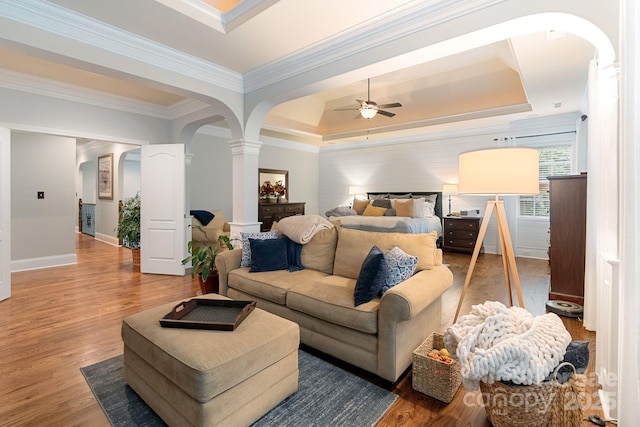 bedroom with arched walkways, decorative columns, wood finished floors, and a raised ceiling