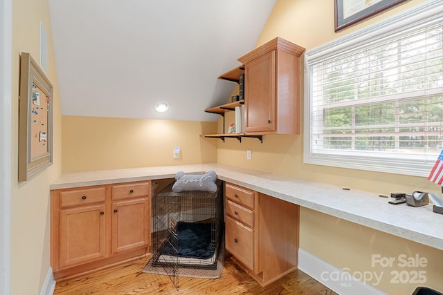 interior space featuring open shelves, built in desk, light countertops, light wood-style flooring, and vaulted ceiling