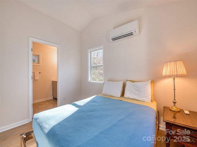 bedroom with lofted ceiling, a wall mounted AC, baseboards, ensuite bath, and wood finished floors