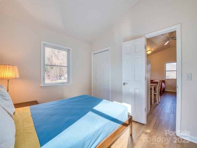 bedroom featuring baseboards, a closet, light wood-type flooring, and vaulted ceiling