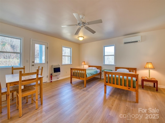 bedroom with baseboards, light wood-style flooring, heating unit, and an AC wall unit