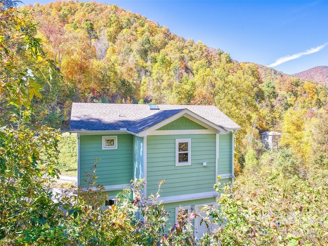 exterior space featuring roof with shingles, a mountain view, and a view of trees