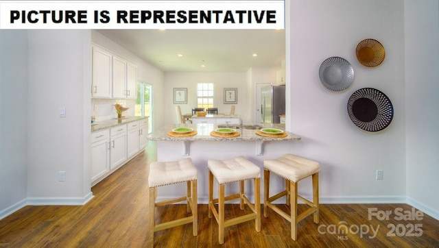 kitchen with dark wood-style flooring, light stone countertops, a breakfast bar, freestanding refrigerator, and white cabinetry
