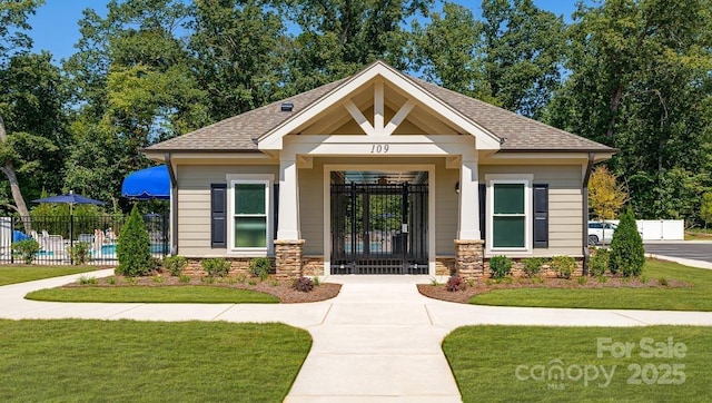 property entrance with a lawn, a shingled roof, fence, and stone siding