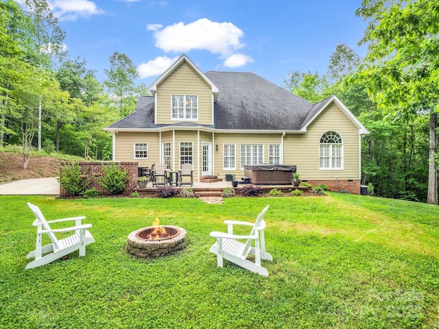 rear view of property featuring a lawn, a hot tub, and an outdoor fire pit