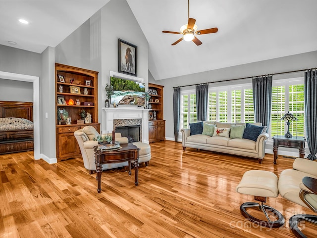 living area featuring a fireplace, baseboards, ceiling fan, high vaulted ceiling, and light wood finished floors