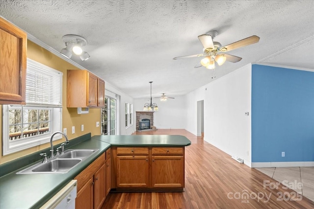 kitchen featuring a peninsula, wood finished floors, a stone fireplace, ceiling fan, and a sink