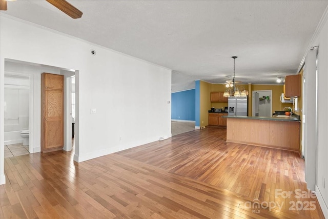 unfurnished living room featuring baseboards, ornamental molding, light wood-style flooring, and ceiling fan with notable chandelier