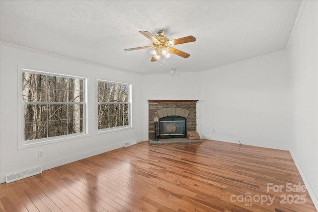 unfurnished living room featuring a ceiling fan, visible vents, a glass covered fireplace, and hardwood / wood-style flooring