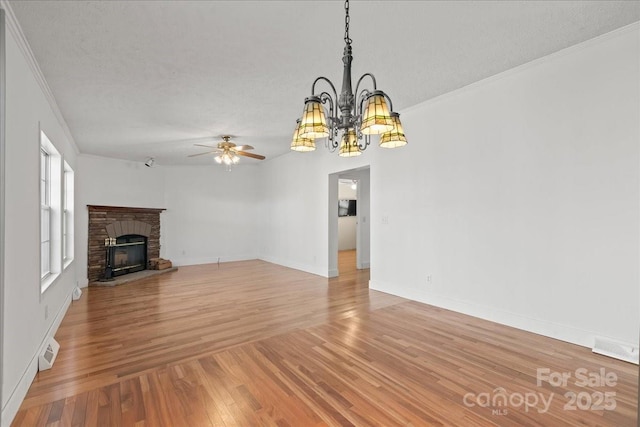 unfurnished living room with crown molding, a fireplace, a textured ceiling, light wood-style flooring, and ceiling fan with notable chandelier