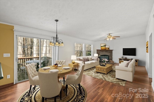 dining space featuring a glass covered fireplace, wood finished floors, baseboards, a textured ceiling, and ceiling fan with notable chandelier