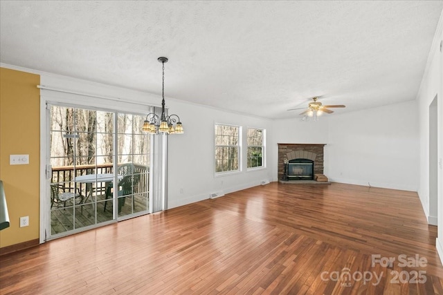 unfurnished living room featuring a stone fireplace, a textured ceiling, baseboards, wood-type flooring, and ceiling fan with notable chandelier
