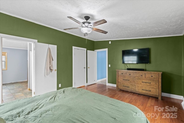 bedroom with crown molding, ceiling fan, a textured ceiling, baseboards, and wood finished floors