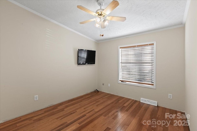 empty room featuring crown molding, ceiling fan, a textured ceiling, wood finished floors, and visible vents