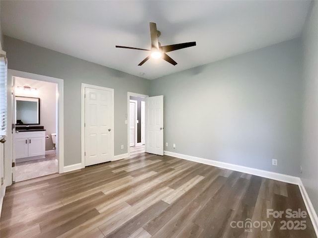 unfurnished bedroom with wood finished floors, baseboards, ensuite bathroom, and ceiling fan