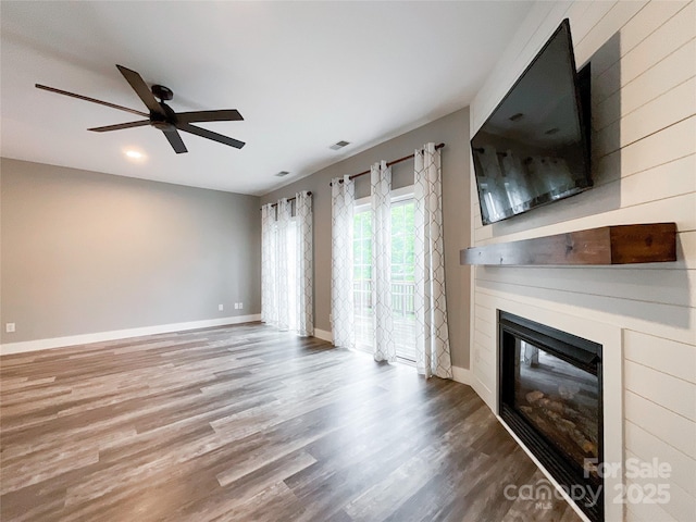 unfurnished living room featuring a glass covered fireplace, ceiling fan, wood finished floors, and baseboards
