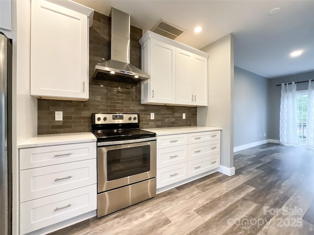kitchen featuring stainless steel electric stove, wall chimney range hood, baseboards, light countertops, and recessed lighting