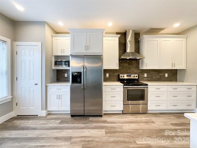 kitchen with appliances with stainless steel finishes, wall chimney range hood, light countertops, white cabinets, and recessed lighting