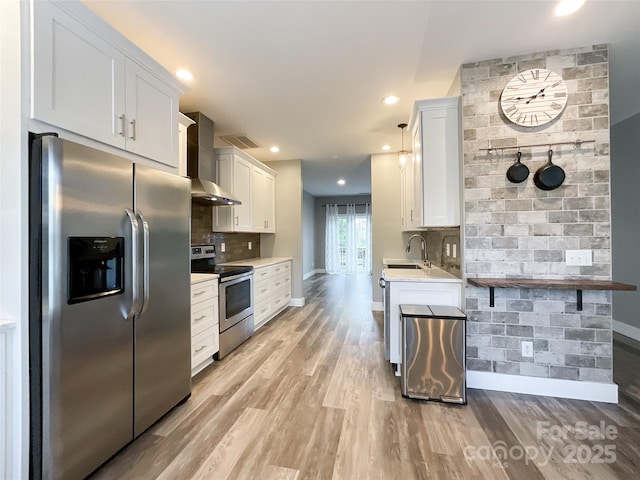 kitchen featuring appliances with stainless steel finishes, wall chimney exhaust hood, light wood-style floors, light countertops, and recessed lighting