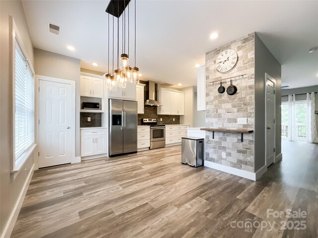 kitchen with stainless steel appliances, wall chimney range hood, light wood finished floors, decorative backsplash, and recessed lighting