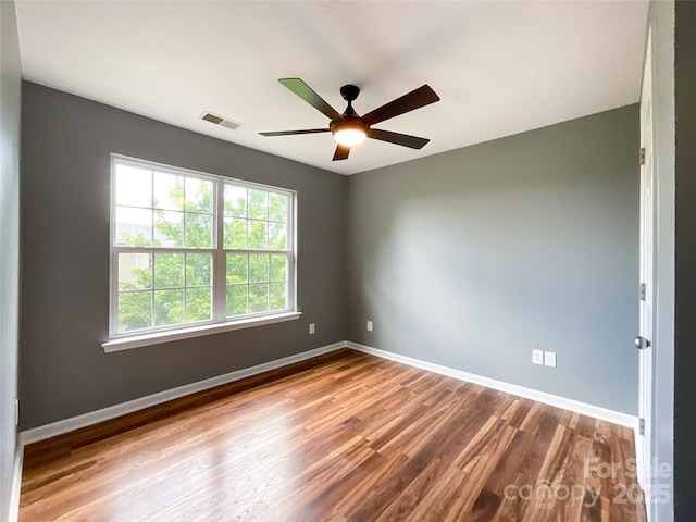 empty room with wood finished floors, a ceiling fan, and baseboards