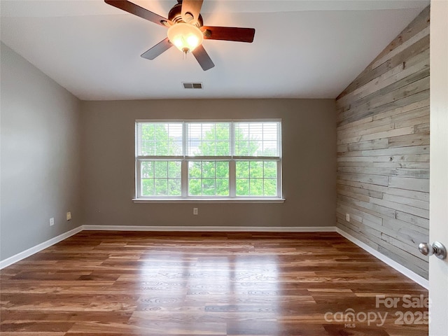 spare room with vaulted ceiling, wood walls, wood finished floors, a ceiling fan, and baseboards