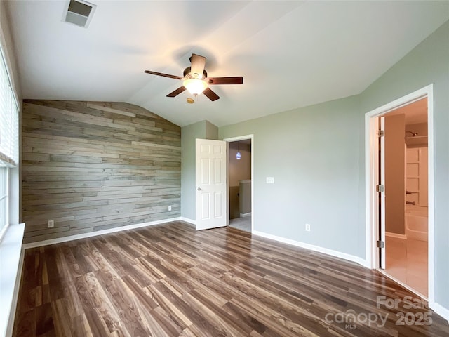 unfurnished bedroom featuring wooden walls, wood finished floors, vaulted ceiling, baseboards, and a ceiling fan