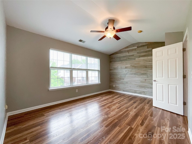 empty room featuring wood walls, lofted ceiling, a ceiling fan, wood finished floors, and baseboards