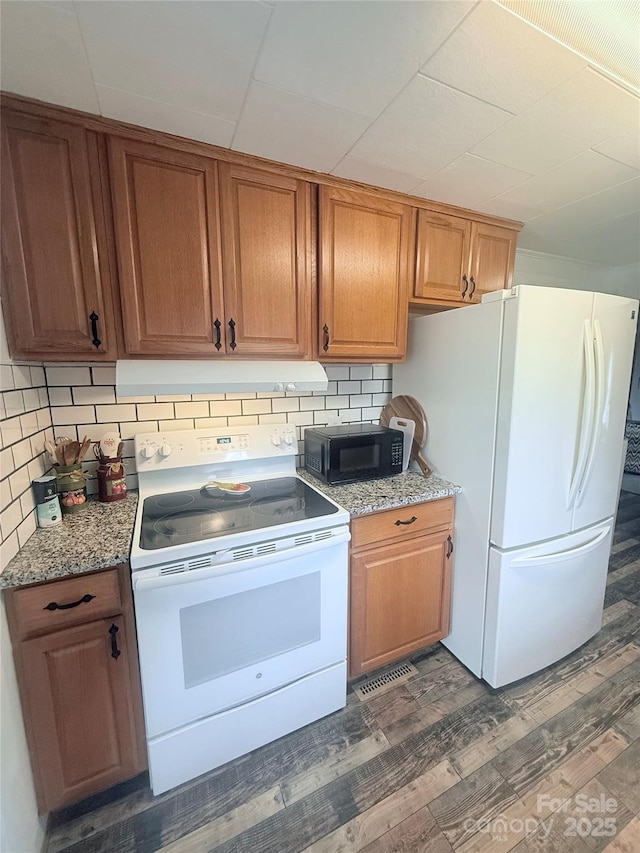 kitchen with white appliances, under cabinet range hood, tasteful backsplash, dark wood-style floors, and light stone counters