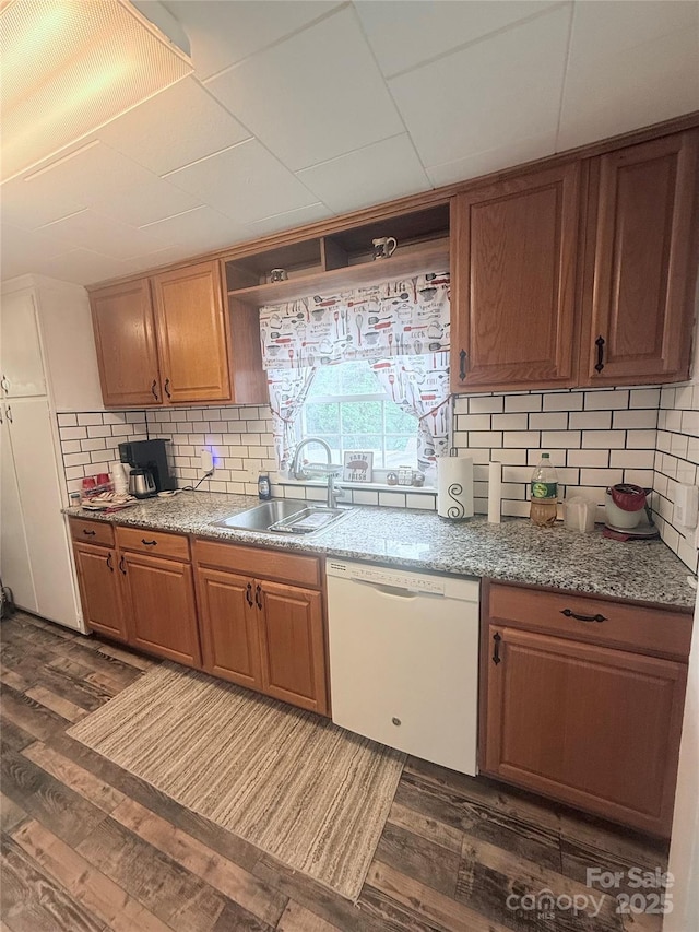 kitchen featuring dishwasher, a sink, dark wood-type flooring, and tasteful backsplash