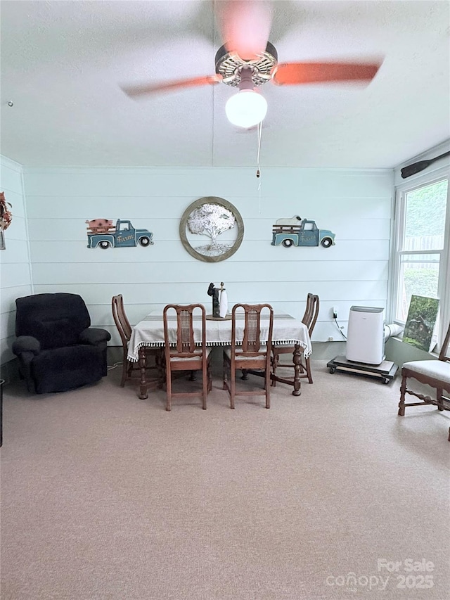 dining space with carpet floors, a ceiling fan, a textured ceiling, and wood walls