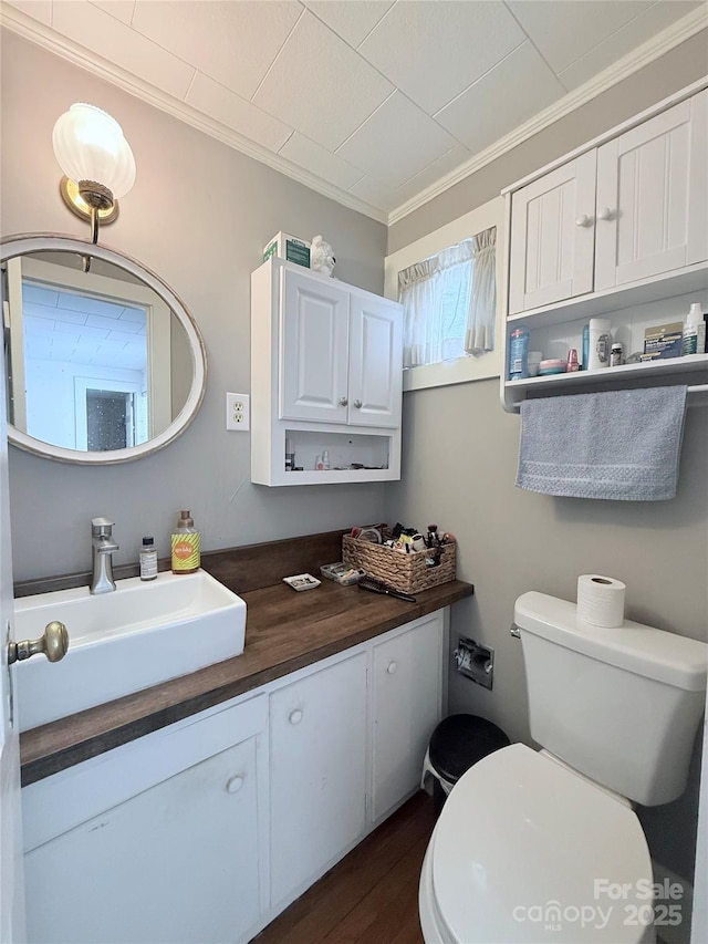 half bath featuring crown molding, toilet, wood finished floors, and vanity