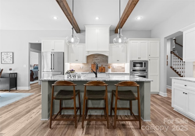 2646 Lee Lawing Rd, Lincolnton, NC 28092 - kitchen featuring appliances with stainless steel finishes, beam ceiling, tasteful backsplash, a kitchen island with sink, and white cabinets