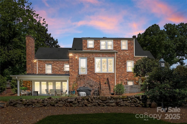 back of house at dusk with a chimney, brick siding, and a patio