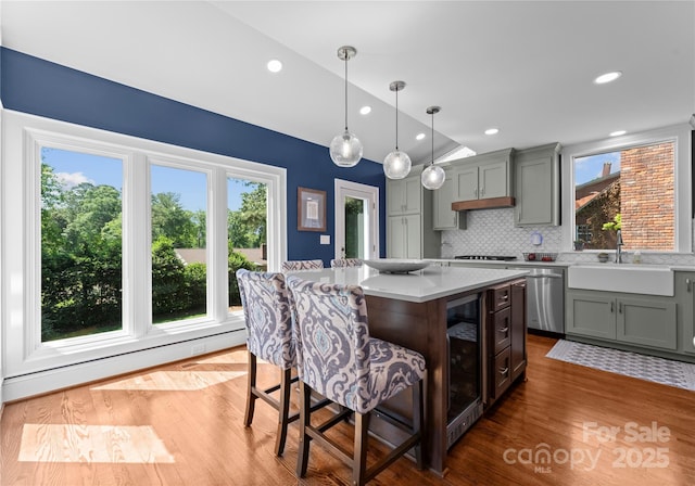 kitchen with appliances with stainless steel finishes, a sink, light countertops, wood finished floors, and beverage cooler