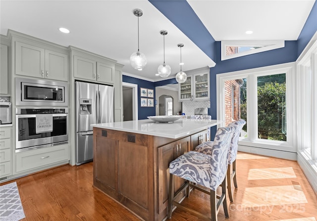 kitchen with appliances with stainless steel finishes, light countertops, a kitchen breakfast bar, wood finished floors, and glass insert cabinets