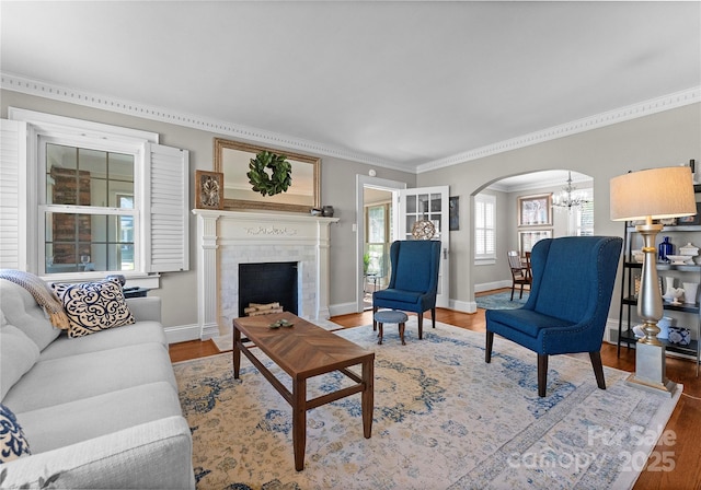 living area featuring arched walkways, crown molding, a chandelier, wood finished floors, and baseboards