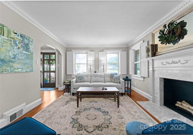 living room with wood finished floors, baseboards, arched walkways, ornamental molding, and a brick fireplace