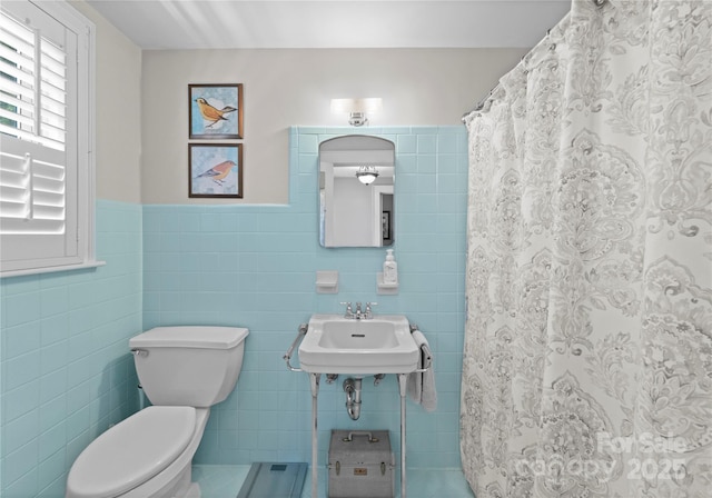full bath featuring tile walls, toilet, wainscoting, curtained shower, and a sink