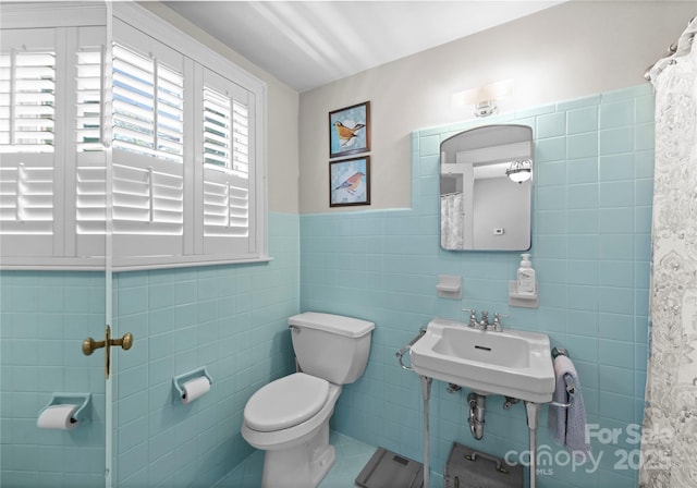 bathroom with tile walls, toilet, a sink, wainscoting, and curtained shower