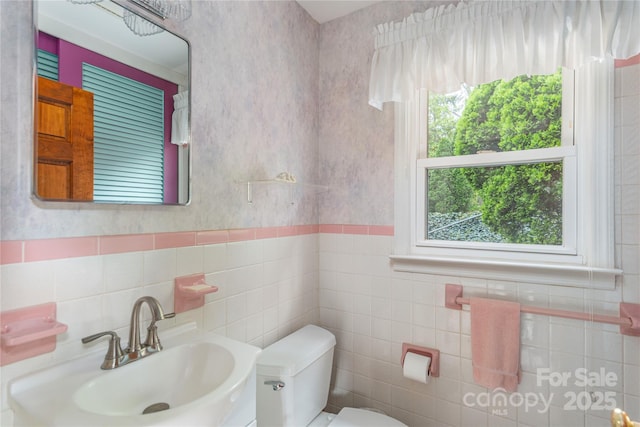 bathroom featuring a sink, tile walls, a wainscoted wall, and toilet